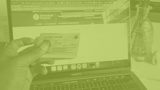 Image of Global Entry Card in hand iin front of a laptop displaying the Trusted Traveler portal